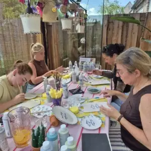 Groep volwassenen glazuurt samen keramiek aan een buitentafel in de tuin