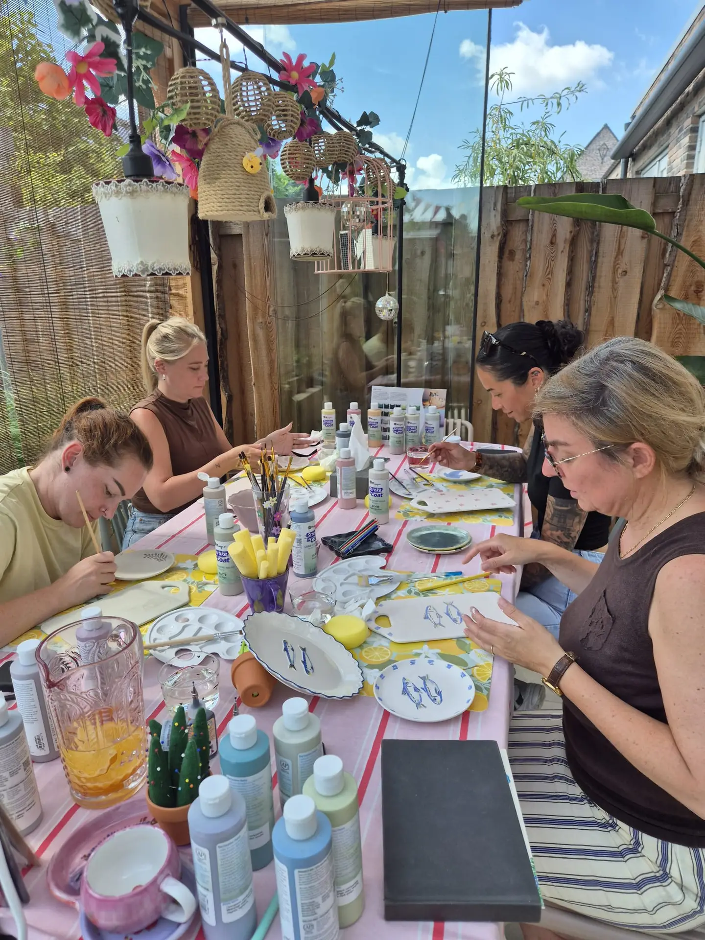 Groep volwassenen glazuurt samen keramiek aan een buitentafel in de tuin