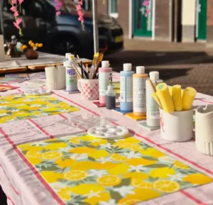 Gedekte workshoptafel met citroentafelkleed, glazuren en penselen