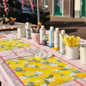 Gedekte workshoptafel met citroentafelkleed, glazuren en penselen
