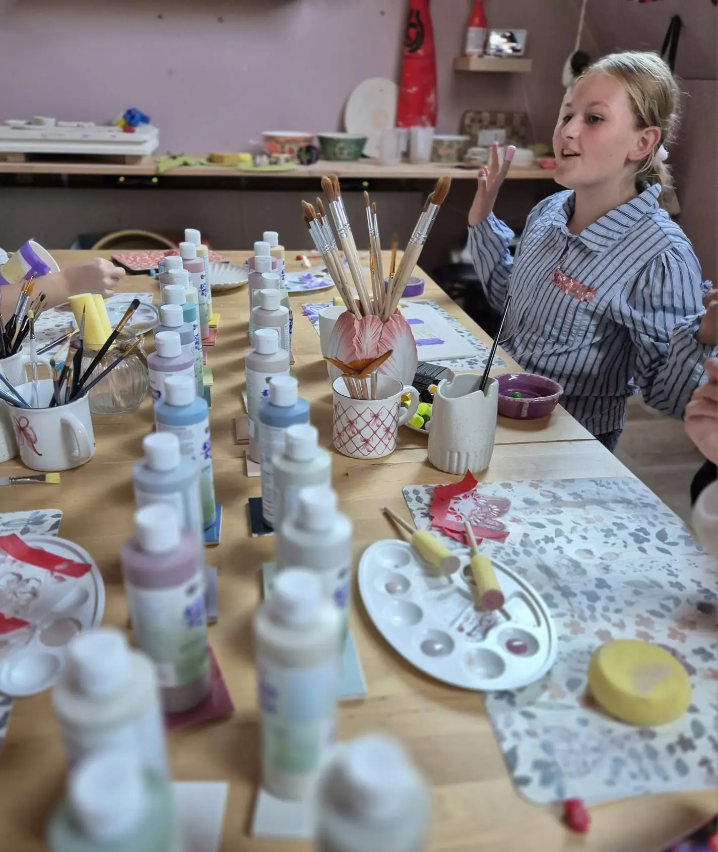 Meisje glazuurt keramiek aan een lange werktafel vol glazuurflessen in De Glazuurkamer